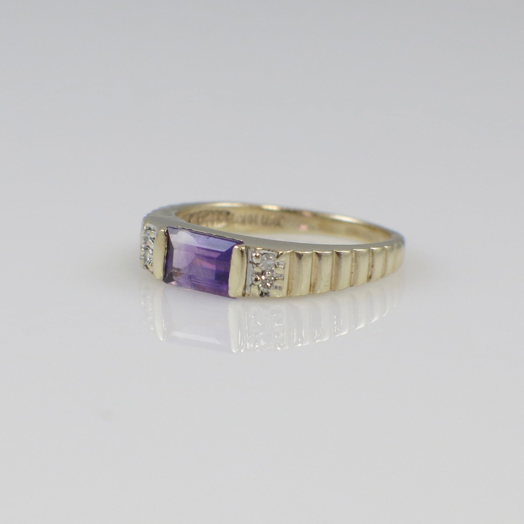 Yellow gold amethyst ring with emerald cut gemstone and diamond accents, featuring a sleek band and intricate detailing.