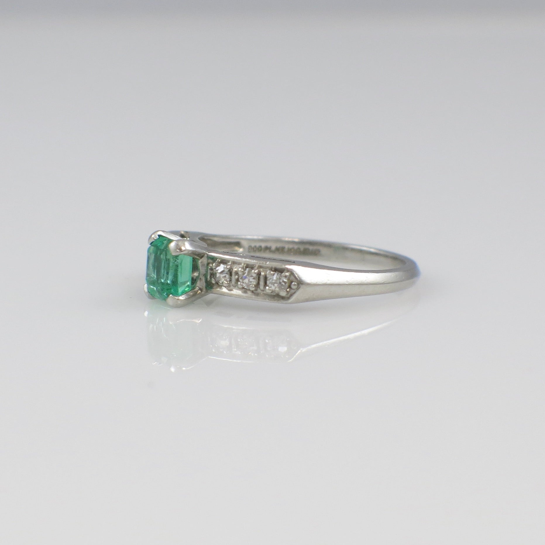 Vintage Art Deco emerald ring with platinum band and diamond accents, circa 1930s, featuring intricate design and detailed craftsmanship.