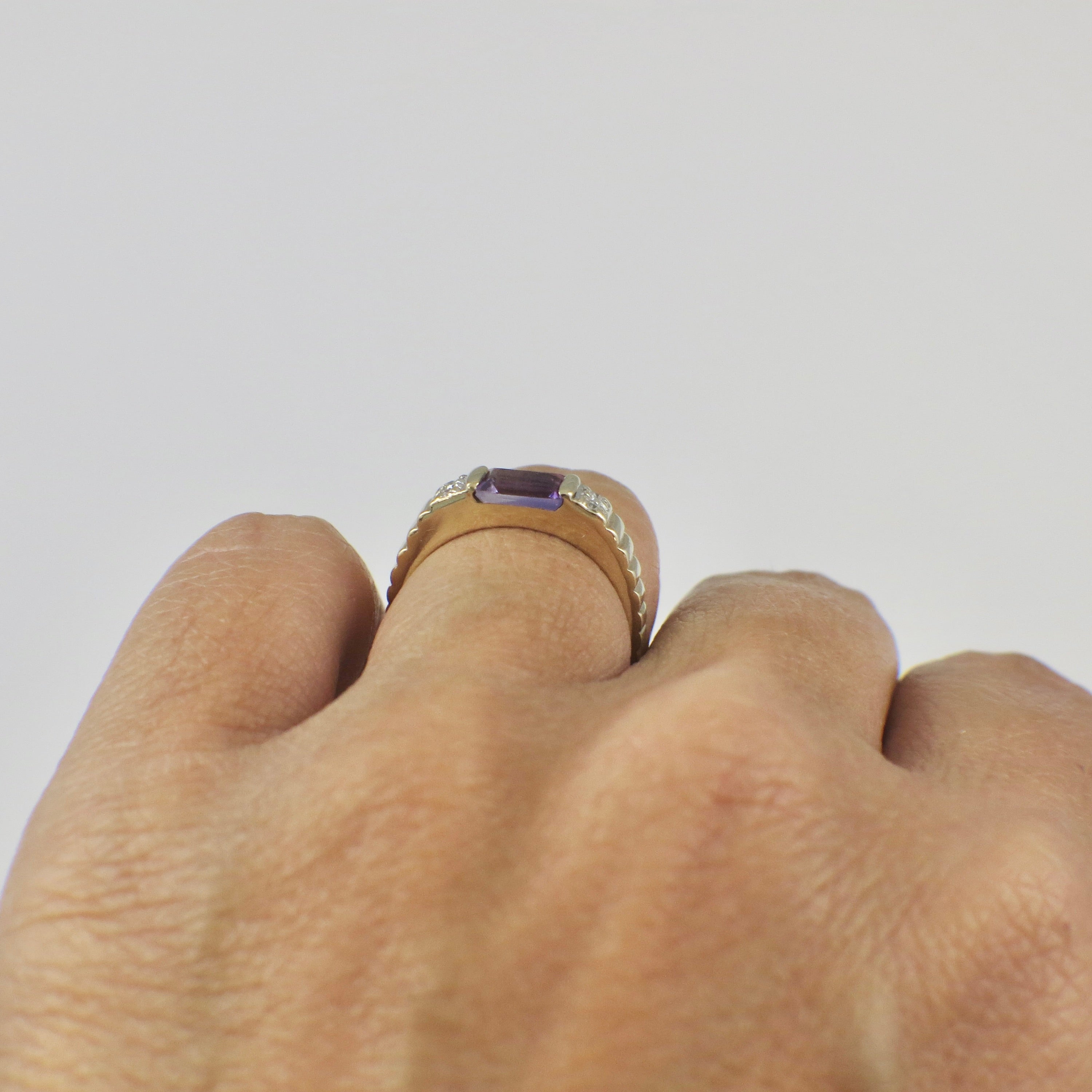 Yellow gold amethyst ring with emerald cut purple stone and diamond accents, showcasing elegant jewelry design.