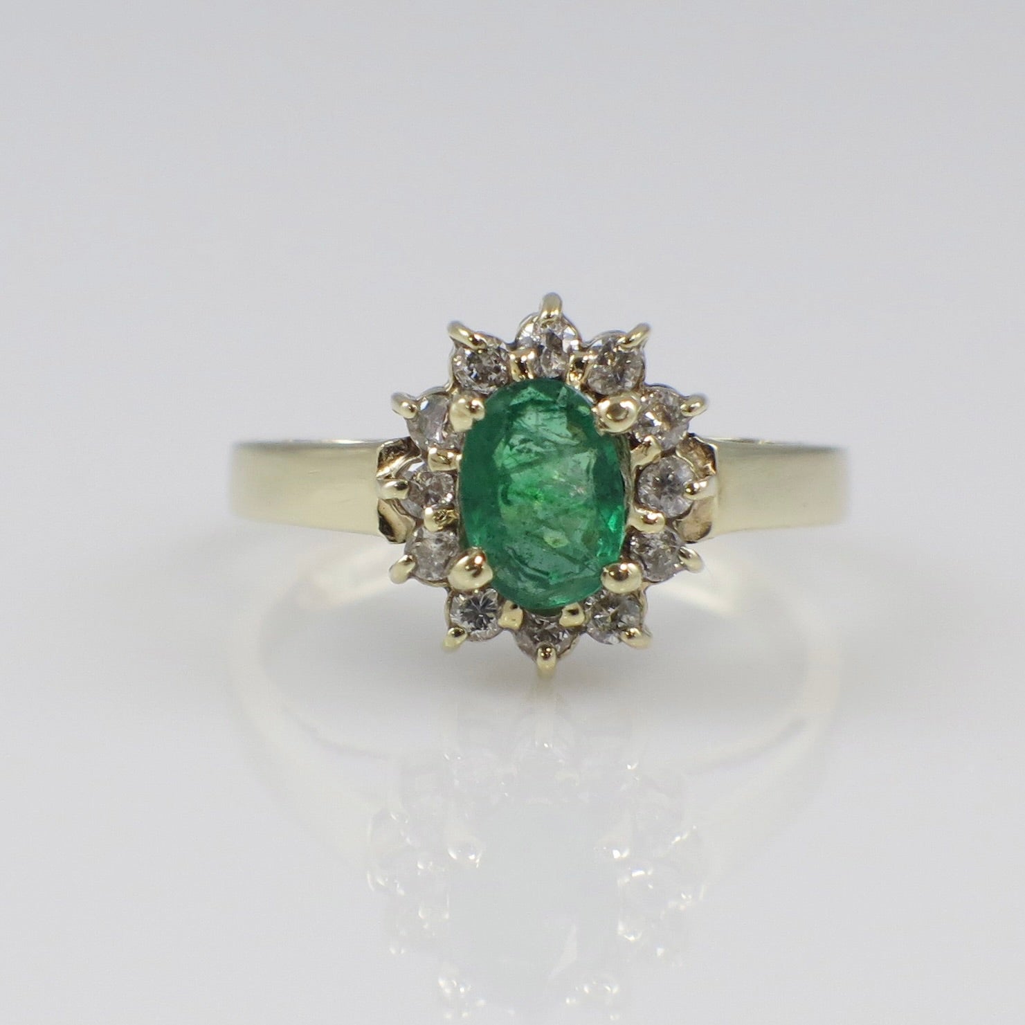 Vintage 14K yellow gold emerald and diamond halo ring with intricate detailing, showcasing a central green emerald surrounded by sparkling diamonds.