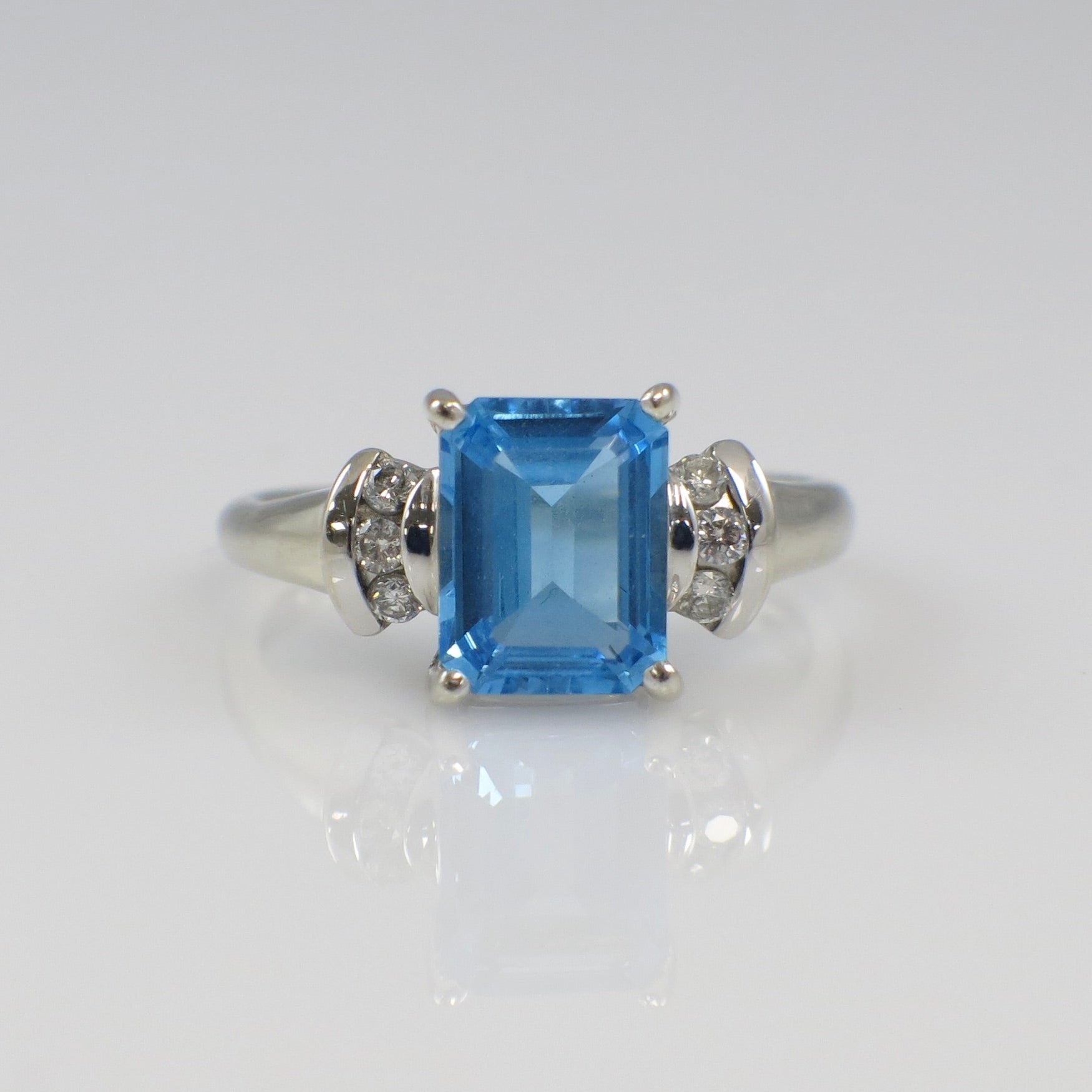 14K white gold blue topaz ring with diamond accents, emerald cut, designed by Black Market LLC, showcasing a sparkling gemstone.