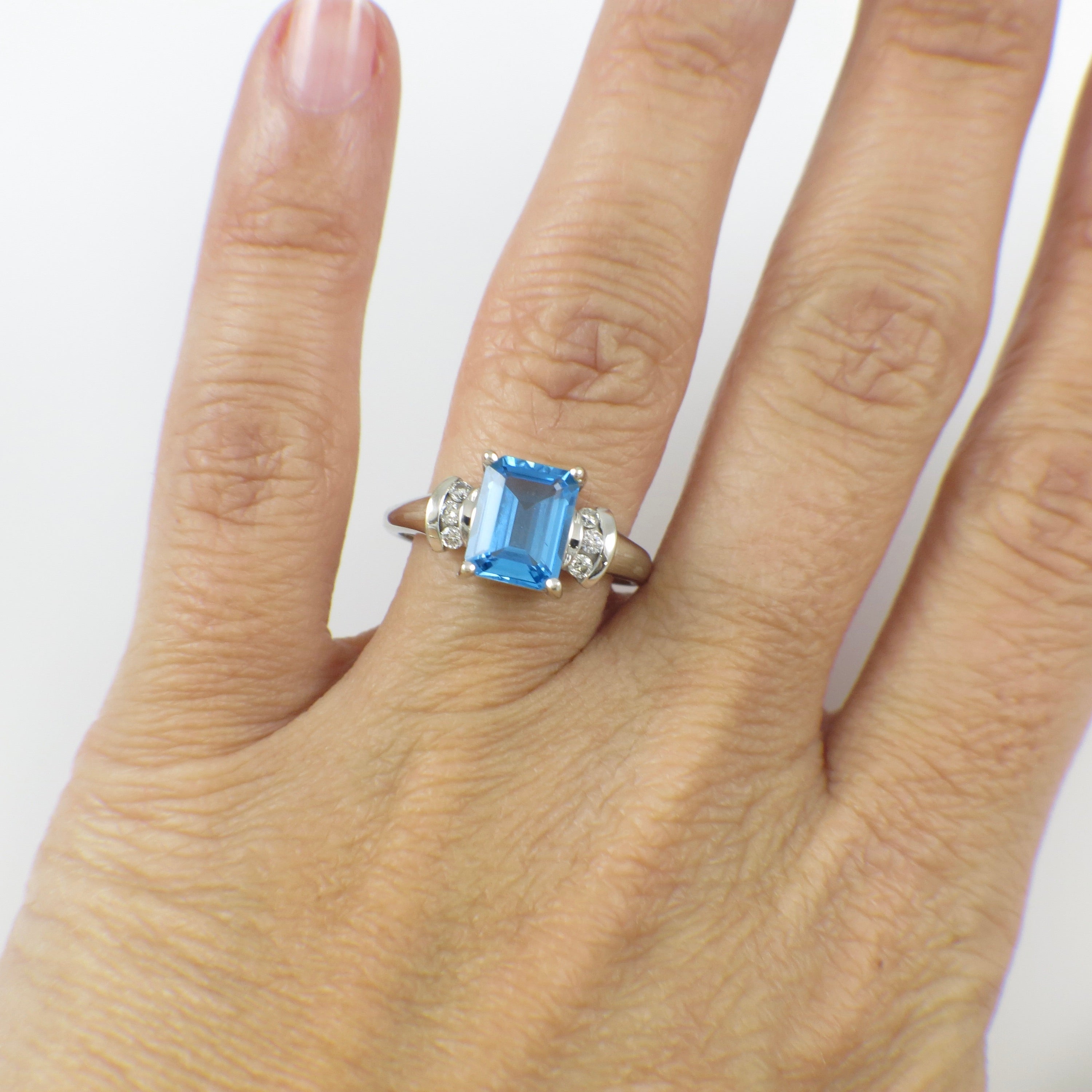 14K white gold blue topaz ring with diamond accents, emerald cut, showcasing a vibrant blue gemstone and sparkling details.