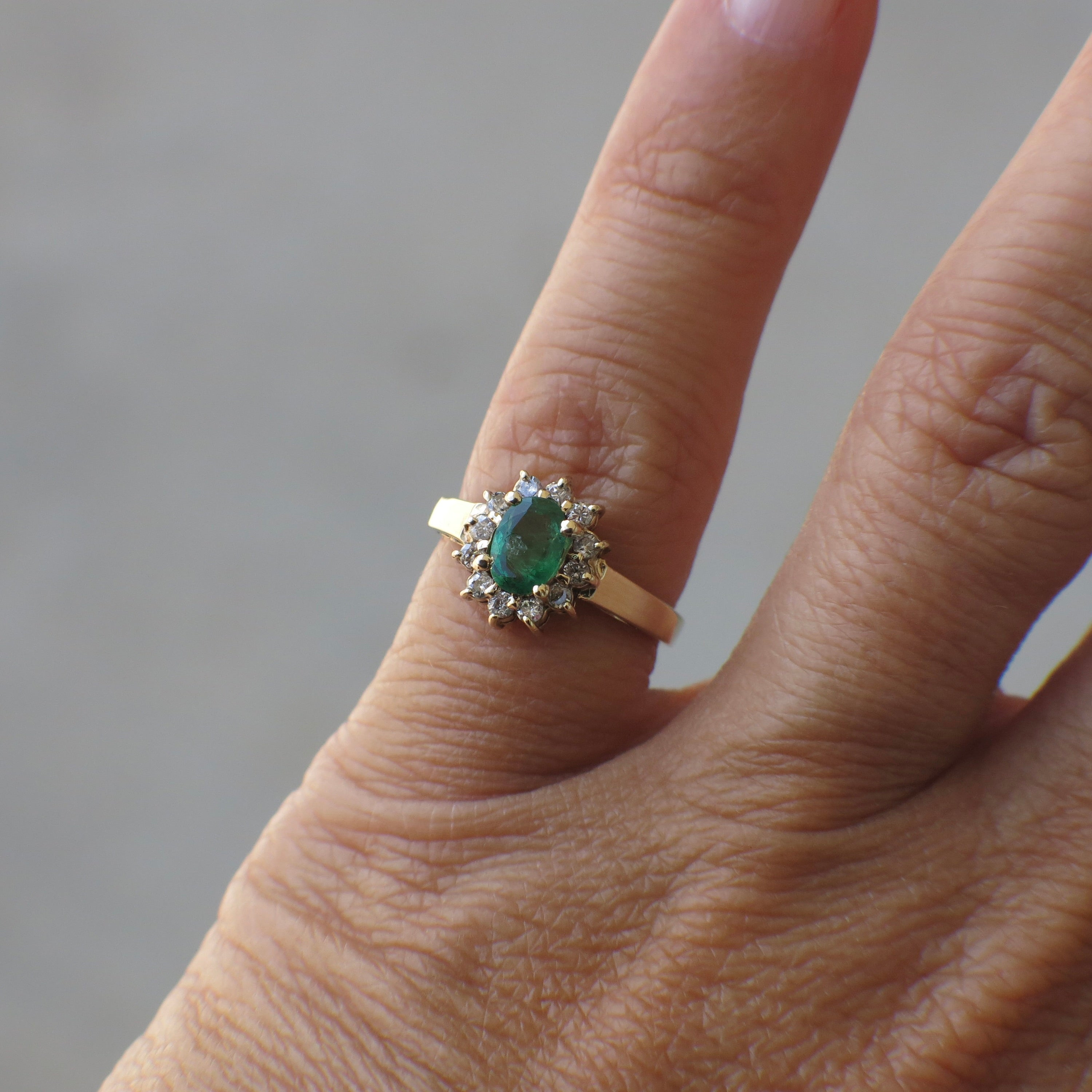 Vintage 14K yellow gold emerald diamond halo ring with intricate detailing, showcasing a central emerald surrounded by sparkling diamonds.