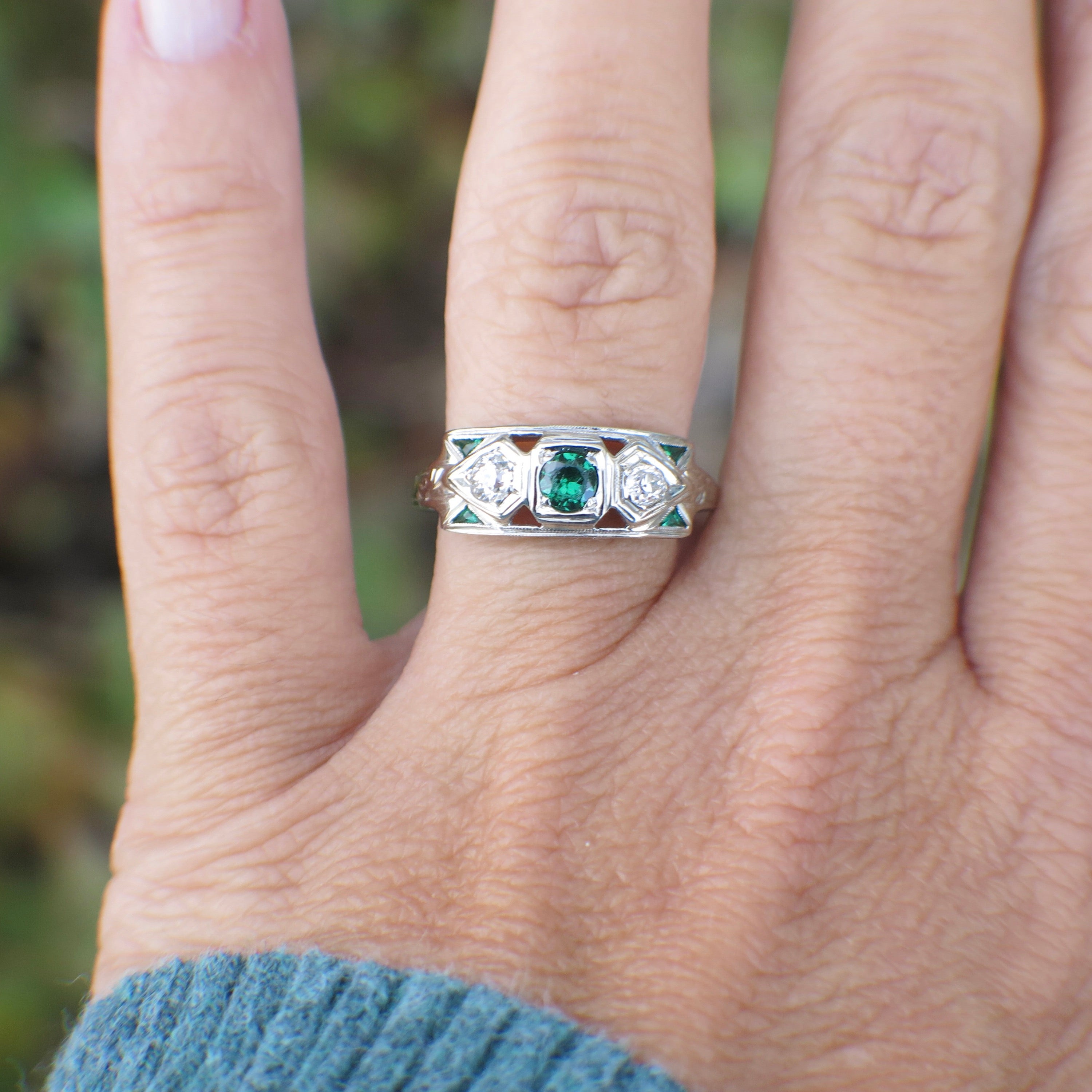 Close-up of a hand wearing a silver ring with green gemstone on a blurred natural background