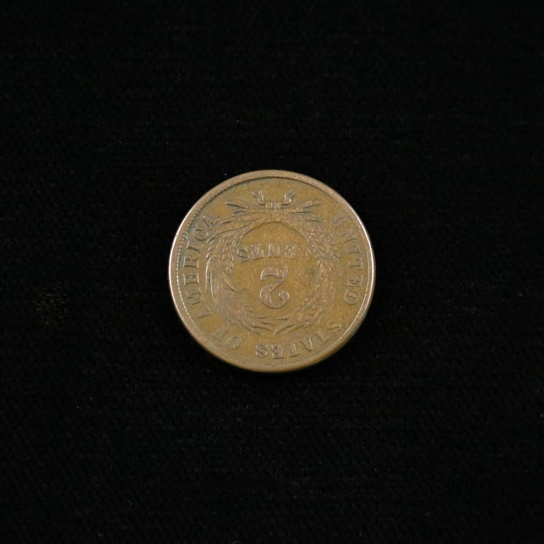 Raw 1864 Two Cent coin with large motto and rotated reverse die, showcasing a rare Civil War-era variety from Black Market LLC.
