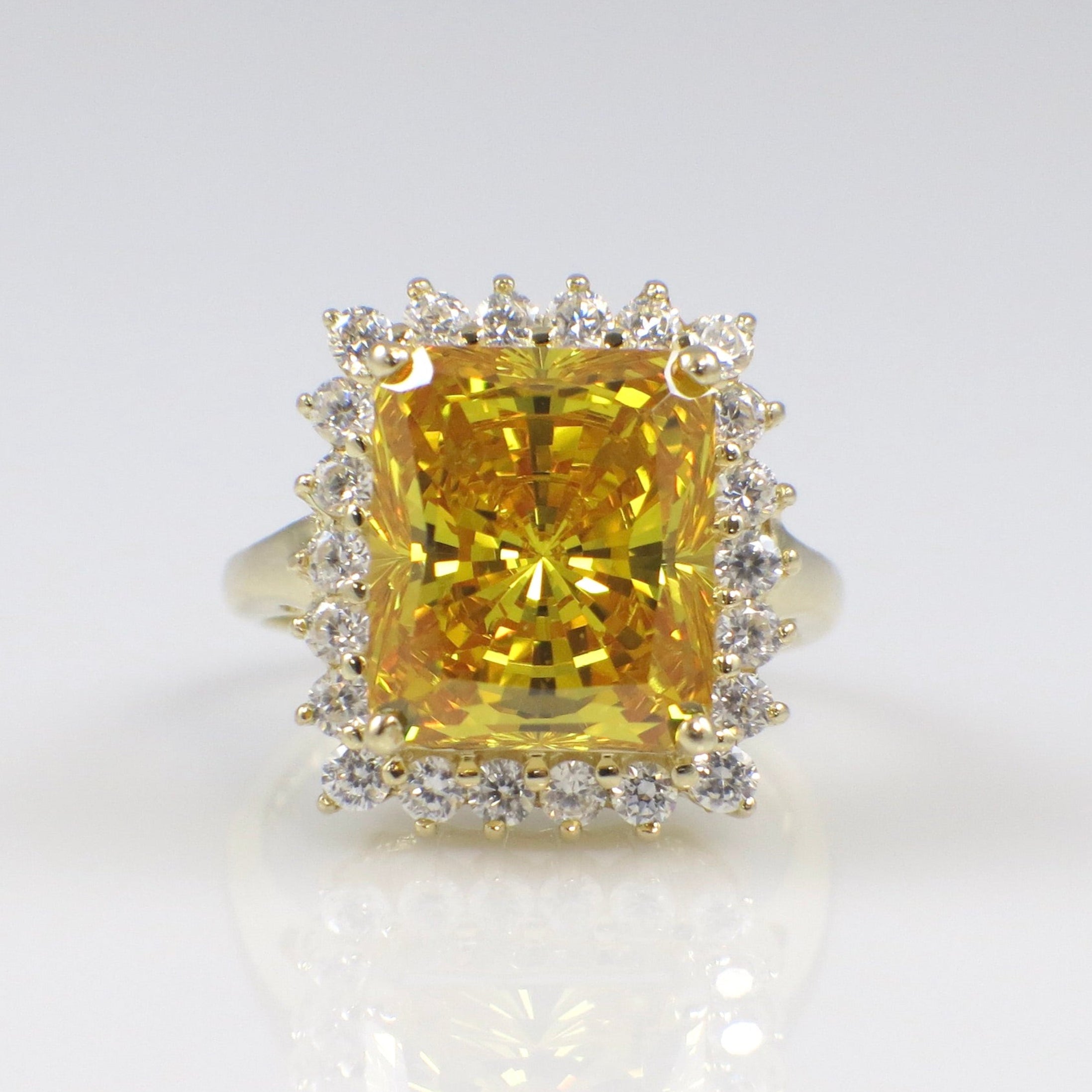 Gold ring with a large yellow gemstone and smaller diamonds on a white background
