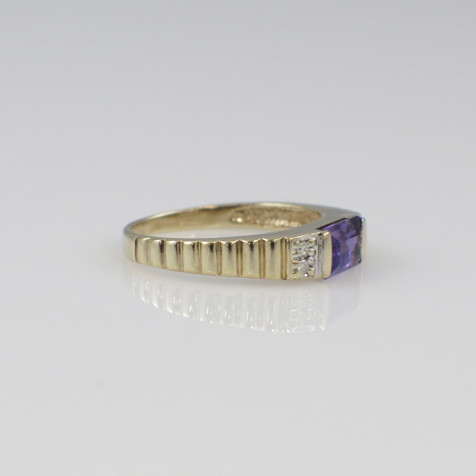 Yellow gold amethyst ring with emerald cut purple gemstone and diamond accents, showcasing elegant jewelry design.
