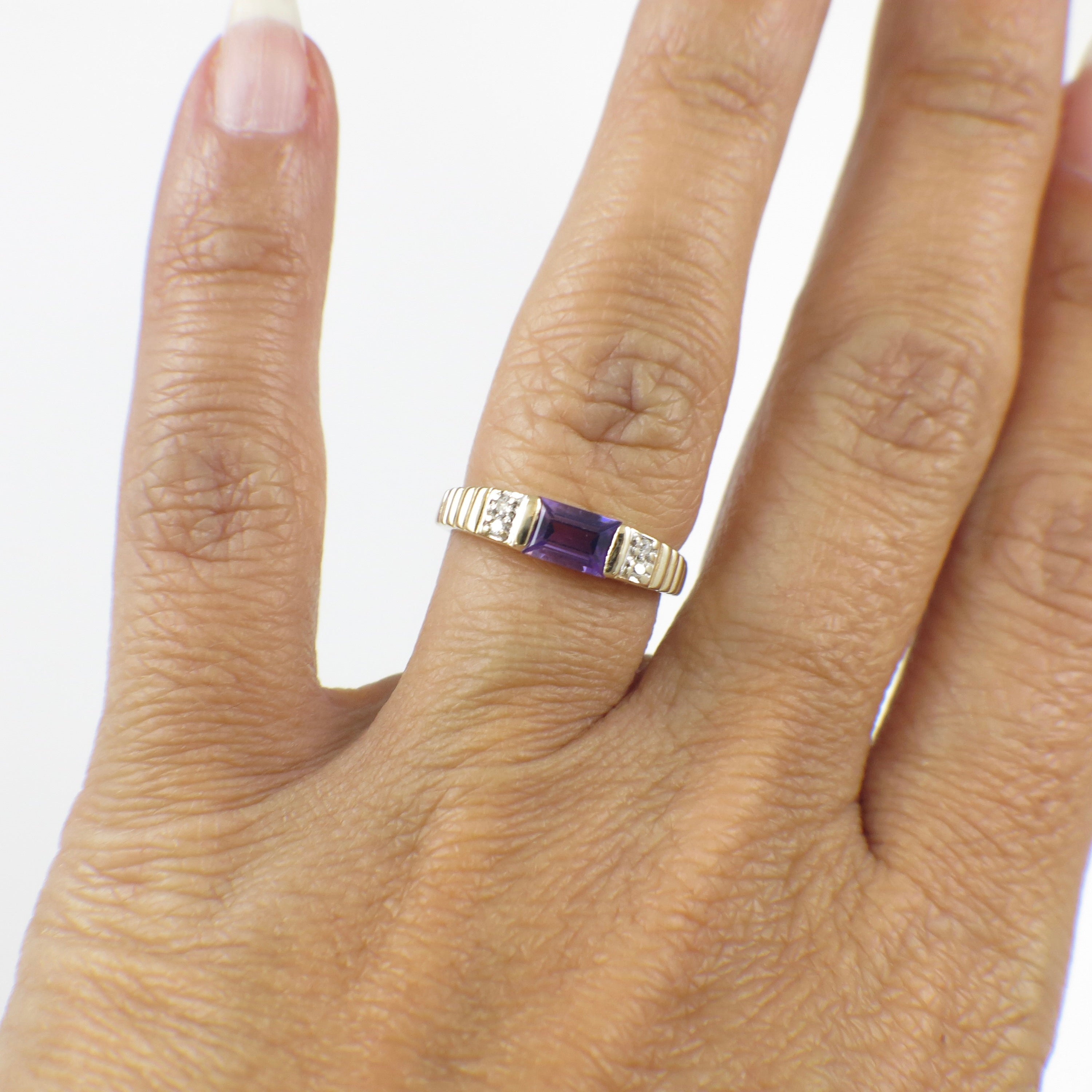 Yellow gold emerald cut amethyst ring with diamond accents, showcasing a luxurious gemstone and intricate band detail.