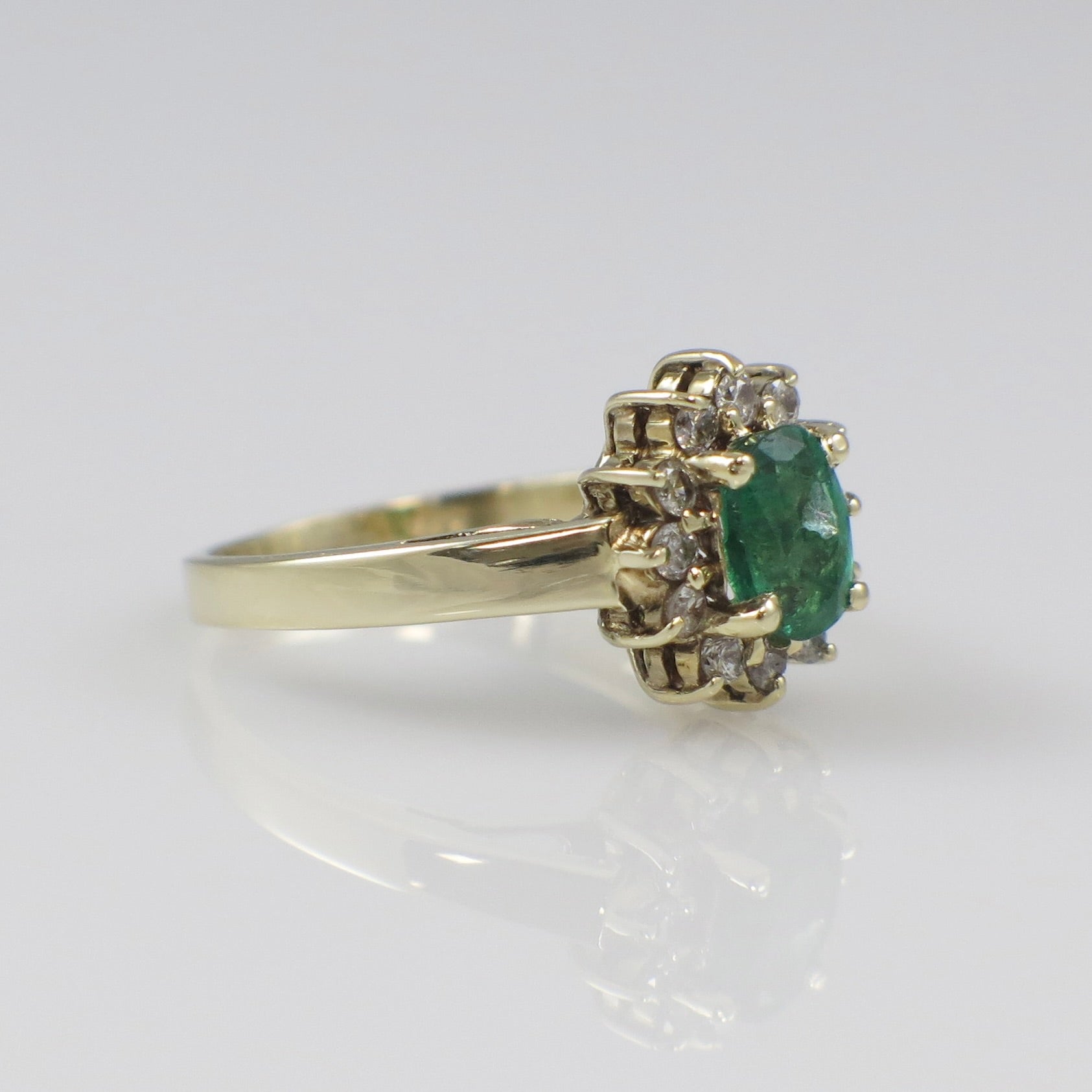 Vintage 14K yellow gold emerald diamond halo ring with intricate design, showcasing a central emerald and surrounding diamonds.