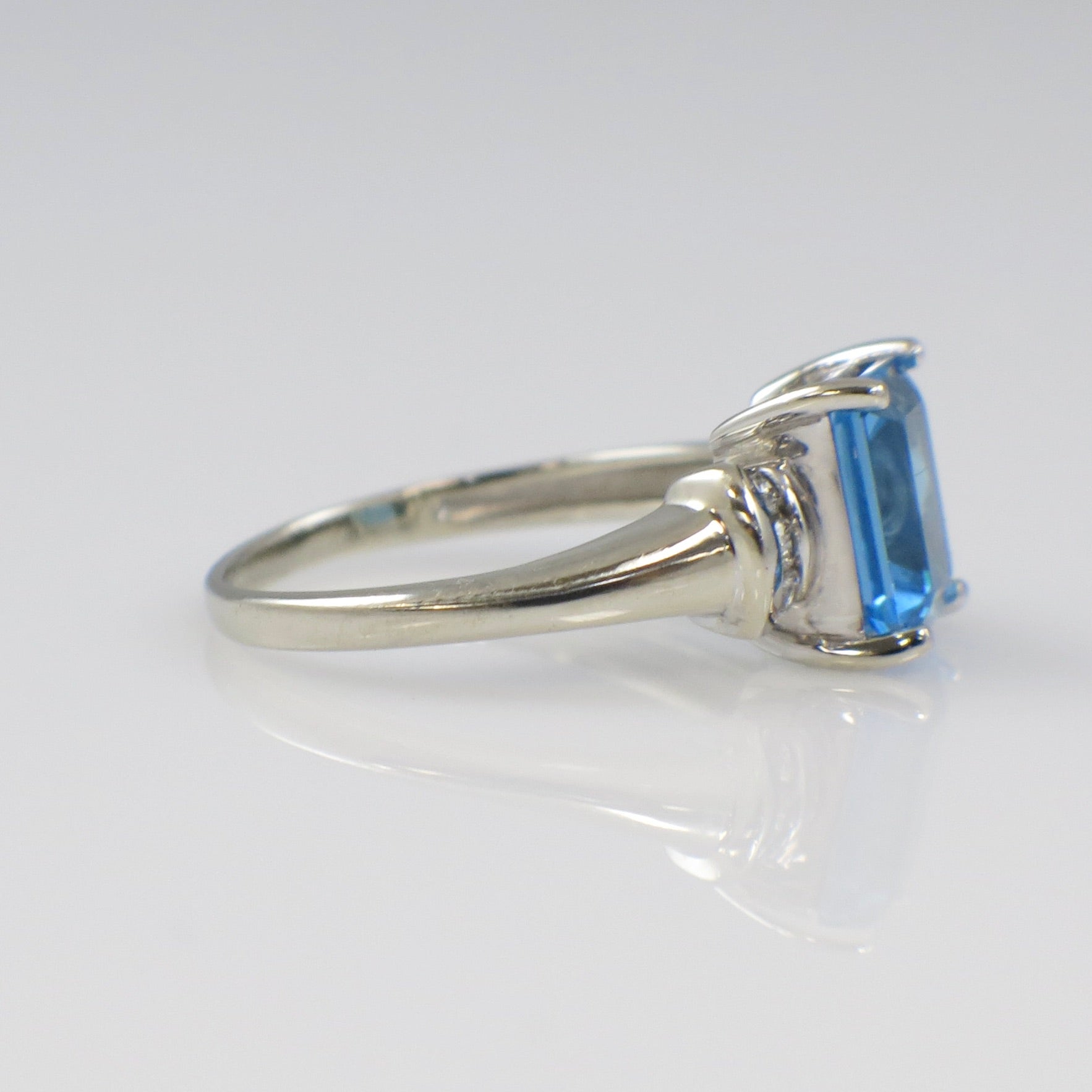 14K white gold blue topaz ring with diamond accents, emerald cut, showcasing a sparkling gemstone and elegant design.