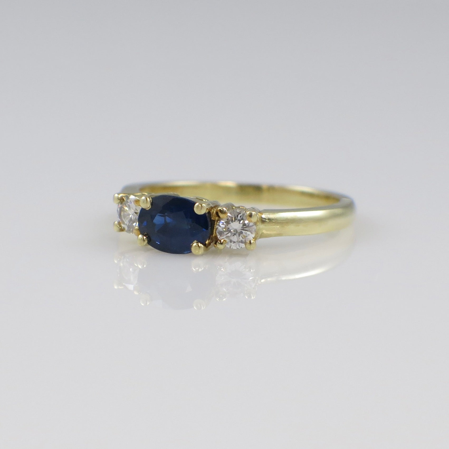 Vintage 18K gold East West sapphire and diamond three-stone ring with black market branding visible on the band.
