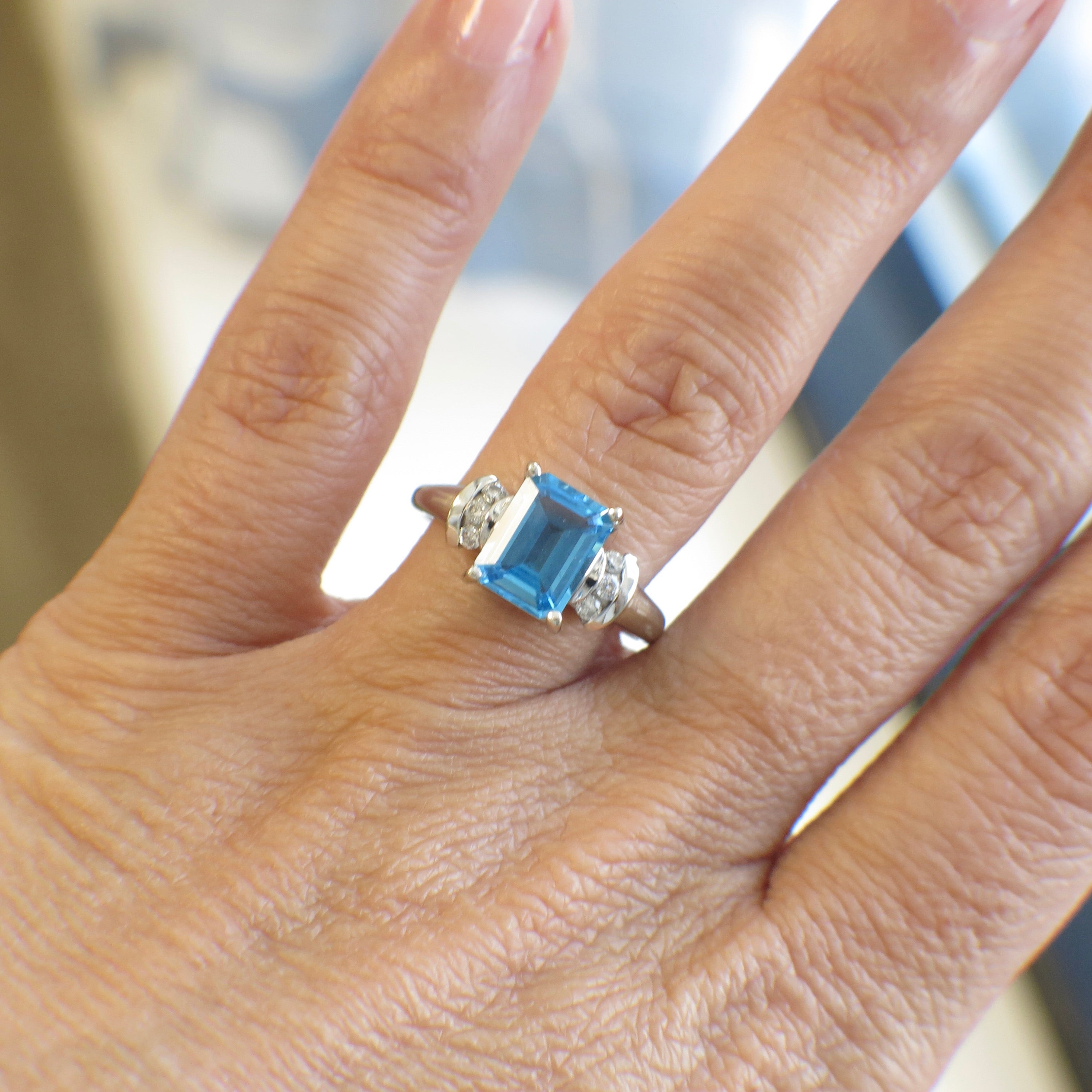 14K white gold blue topaz ring with diamond accents, emerald cut, featuring a large central blue gemstone and sparkling side diamonds.
