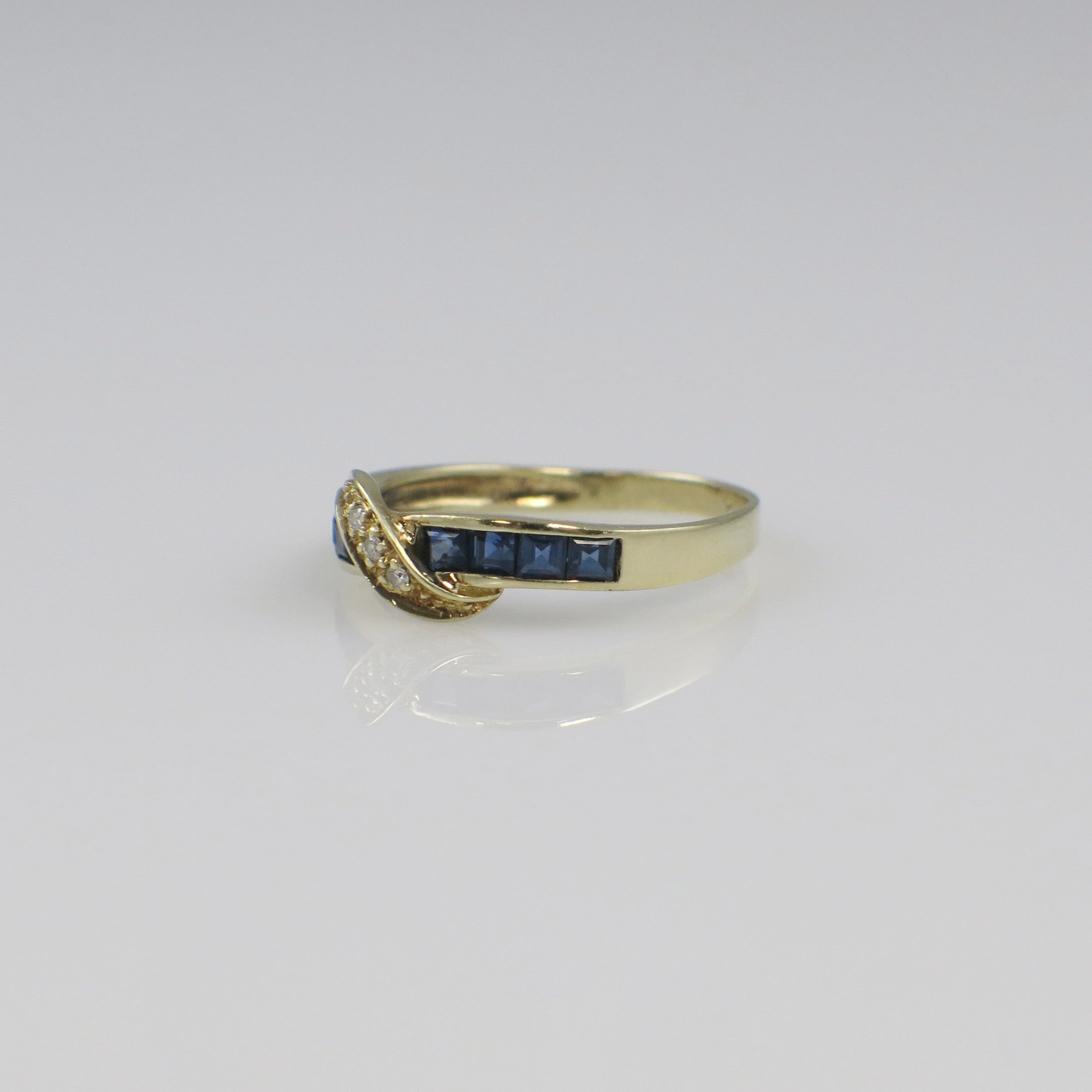 Vintage 14K yellow gold sapphire and diamond bypass ring with intricate design, featuring a central blue sapphire and sparkling diamonds.