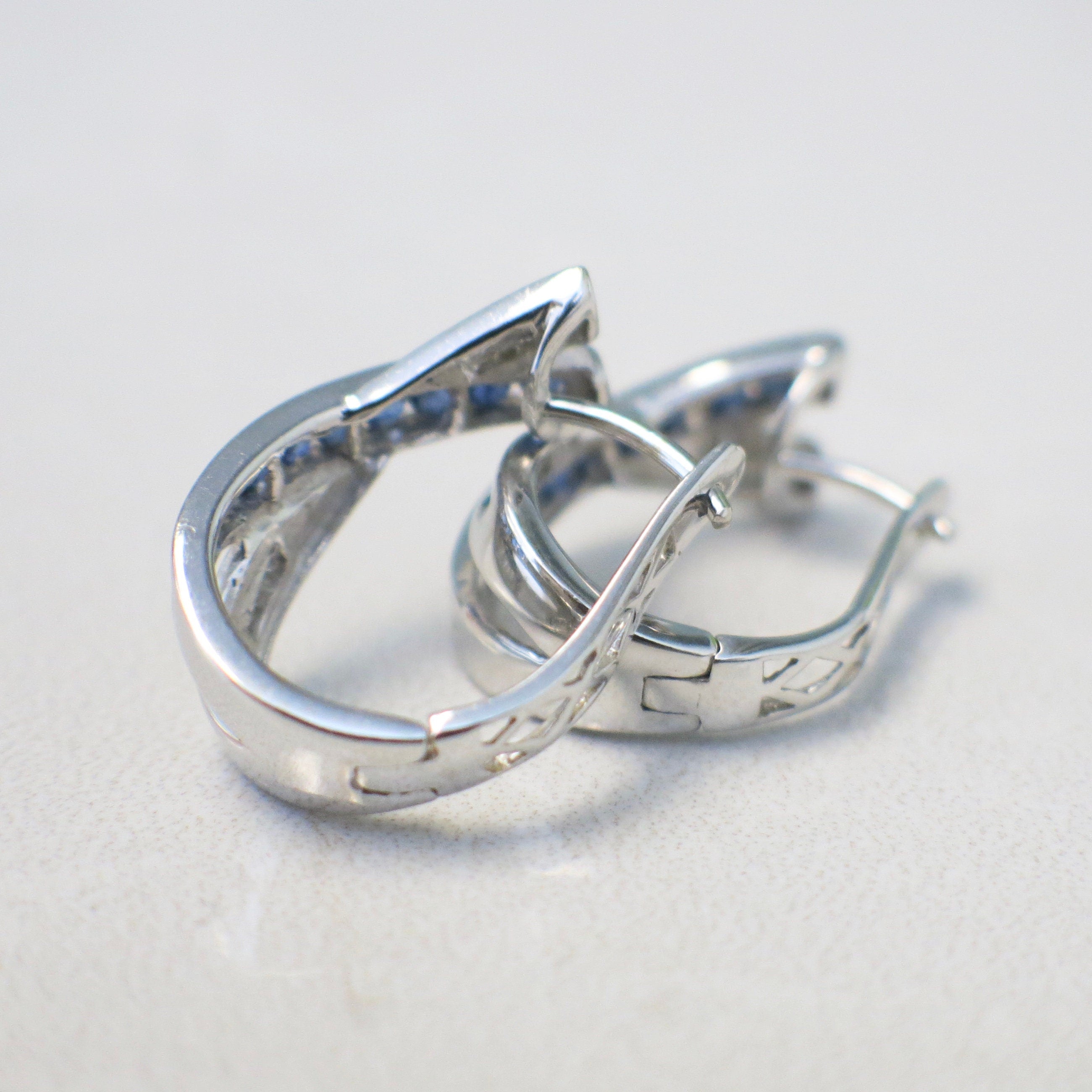 14K white gold sapphire and diamond hoop earrings with an X design, princess cut sapphires, and baguette diamonds.