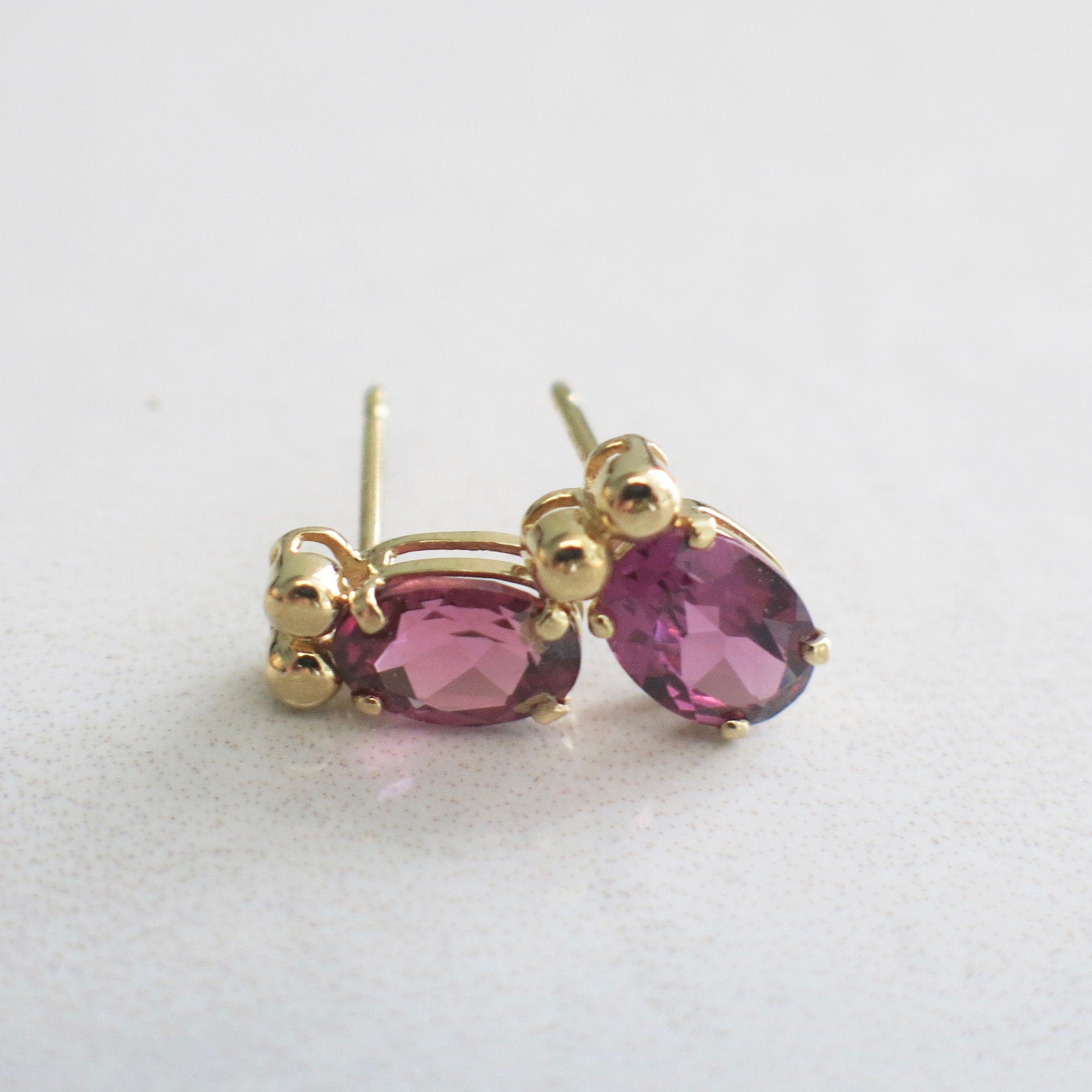 14K yellow gold Rhodolite Garnet earrings with oval 7x5 mm studs, featuring vibrant red-purple gemstones and classic stud design.