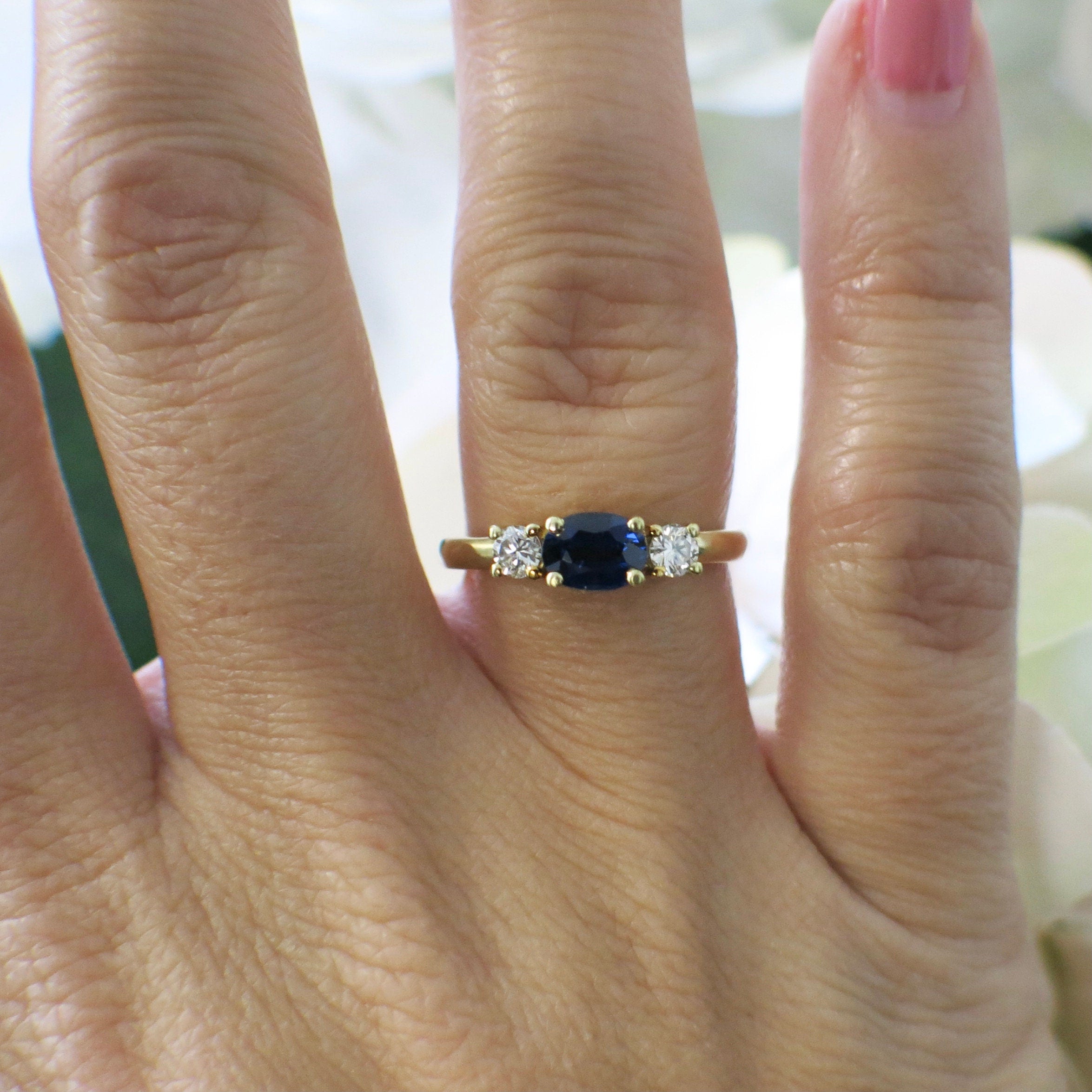 18K yellow gold sapphire and diamond three-stone ring with east-west design, featuring a central sapphire flanked by diamonds.