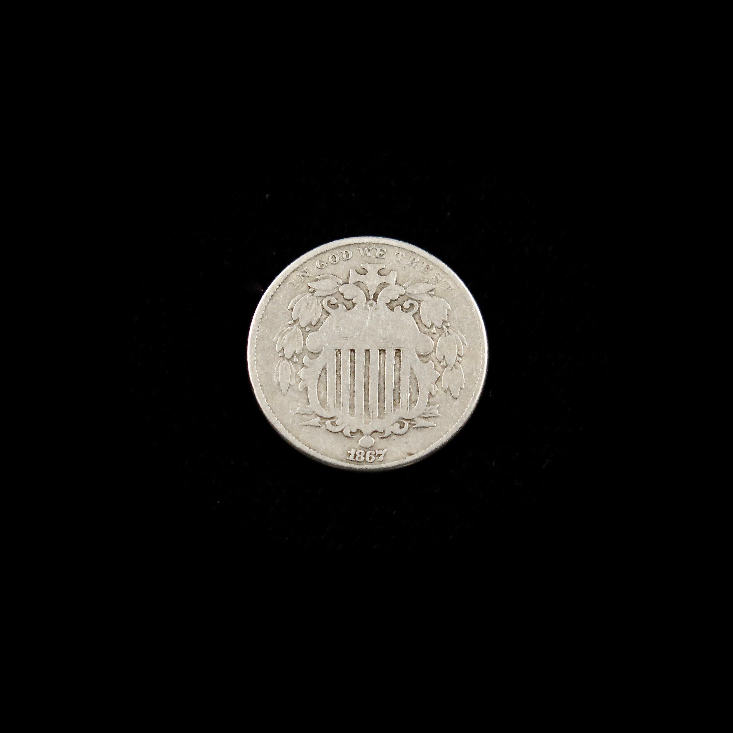 1867 Shield Nickel U.S. five-cent coin with no rays on reverse, raw condition, featuring shield design and "Good" grade.
